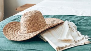 A neatly made bed with a green bedspread, a woven hat, and a folded cloth on the bed. - Casa du Soleil Hostal Boutique (Madrid)