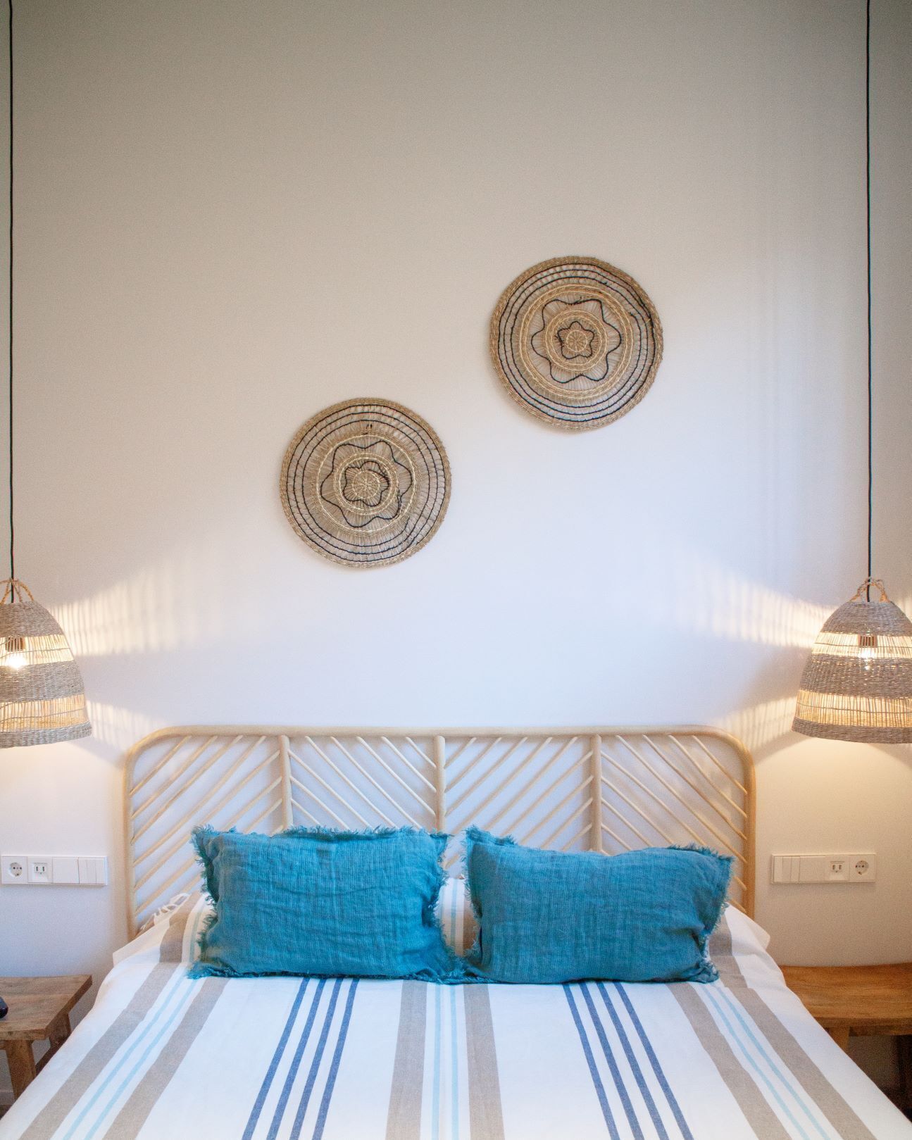 Una cama con colcha a rayas, dos almohadas azules y un cabecero tejido.