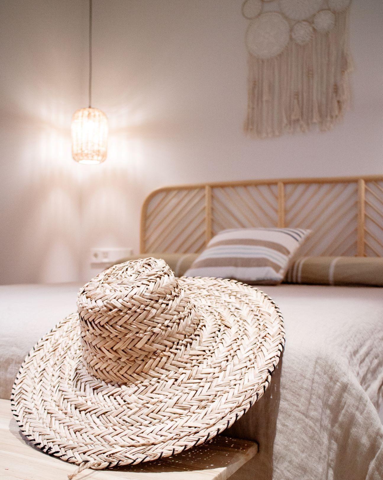 A bed with a woven basket hat, a bedside lamp, and a wall with a dreamcatcher.