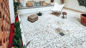 A spacious outdoor area with a tiled floor, a seating area with cushions, a white chair, and a small table. - Casa du Soleil Hostal Boutique (Madrid)