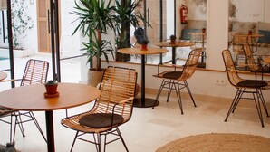 A cafe with wicker chairs, round tables, and potted plants. - Casa du Soleil Hostal Boutique (Madrid)