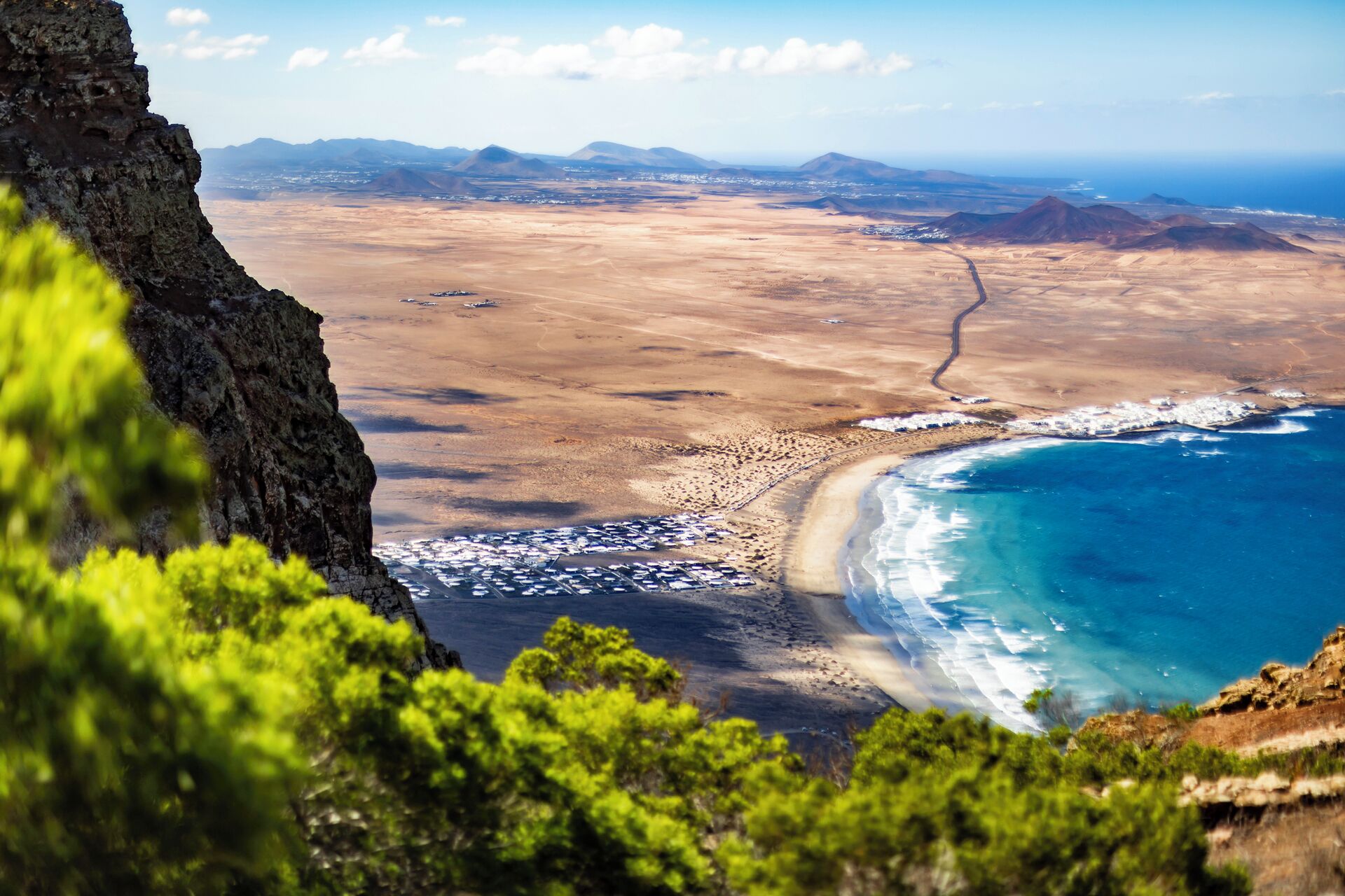 A coastal landscape with a beach, rocky cliffs, and distant mountains.