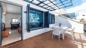 A modern apartment with a terrace featuring a dining area, a potted plant, and a view of the city.