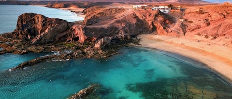 A coastal landscape with a rocky shoreline, clear turquoise waters, and a distant mountain.