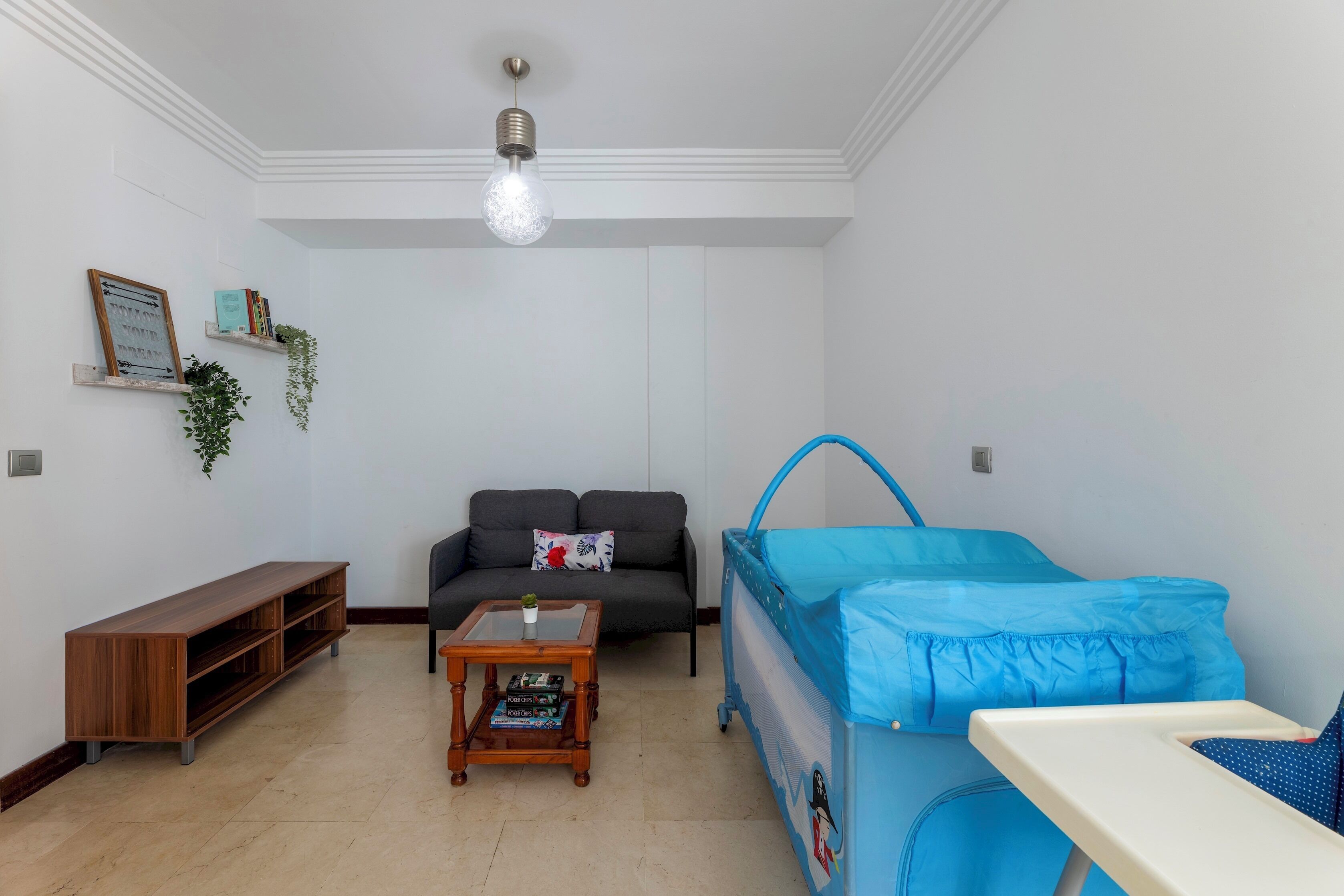 A living room with a sofa, a coffee table, a bookshelf, a baby crib, and a ceiling light.