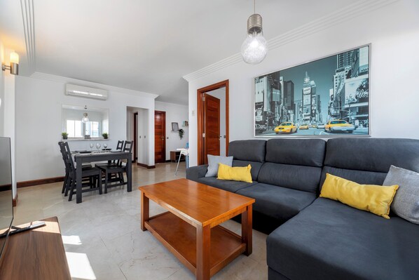 A modern living room with a dark grey sofa, wooden coffee table, and a cityscape painting on the wall.