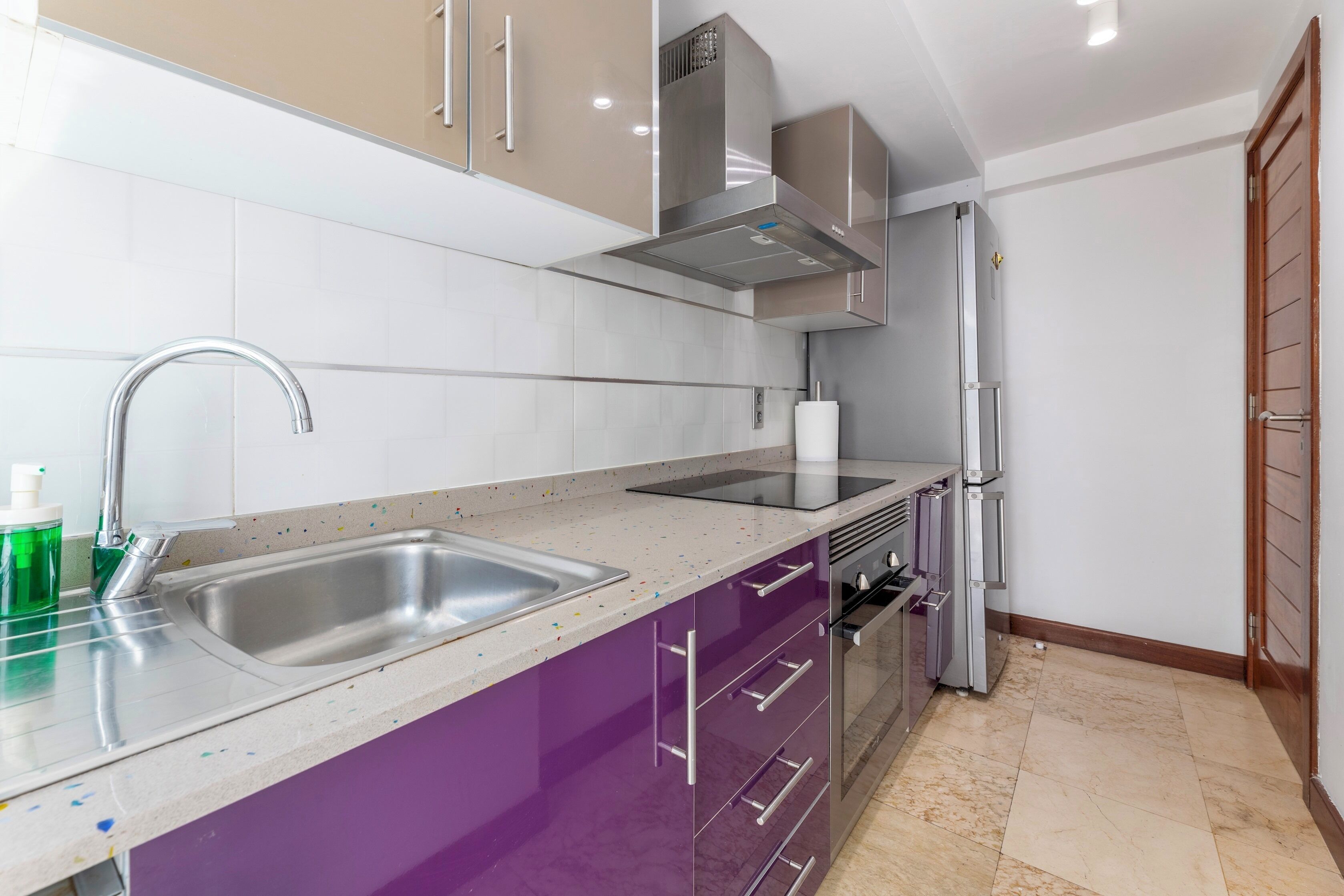 Una cocina moderna con electrodomésticos de acero inoxidable, un lavamanos doble y un armario morado.
