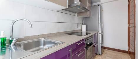 Una cocina moderna con electrodomésticos de acero inoxidable, un lavamanos doble y un armario morado.