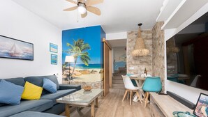 Un salon moderne agrémenté d’une fresque murale représentant une plage, d’un ventilateur de plafond, d’un coin repas avec des chaises et d’un mur d’accent en pierre.