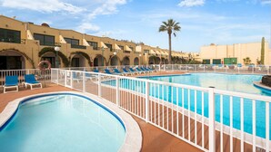 Un espace piscine comprenant plusieurs bassins et des chaises longues, le tout entouré d’une clôture blanche.