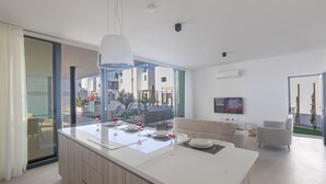 A modern kitchen with a large island, dining area with chairs, a sofa, and a TV.
