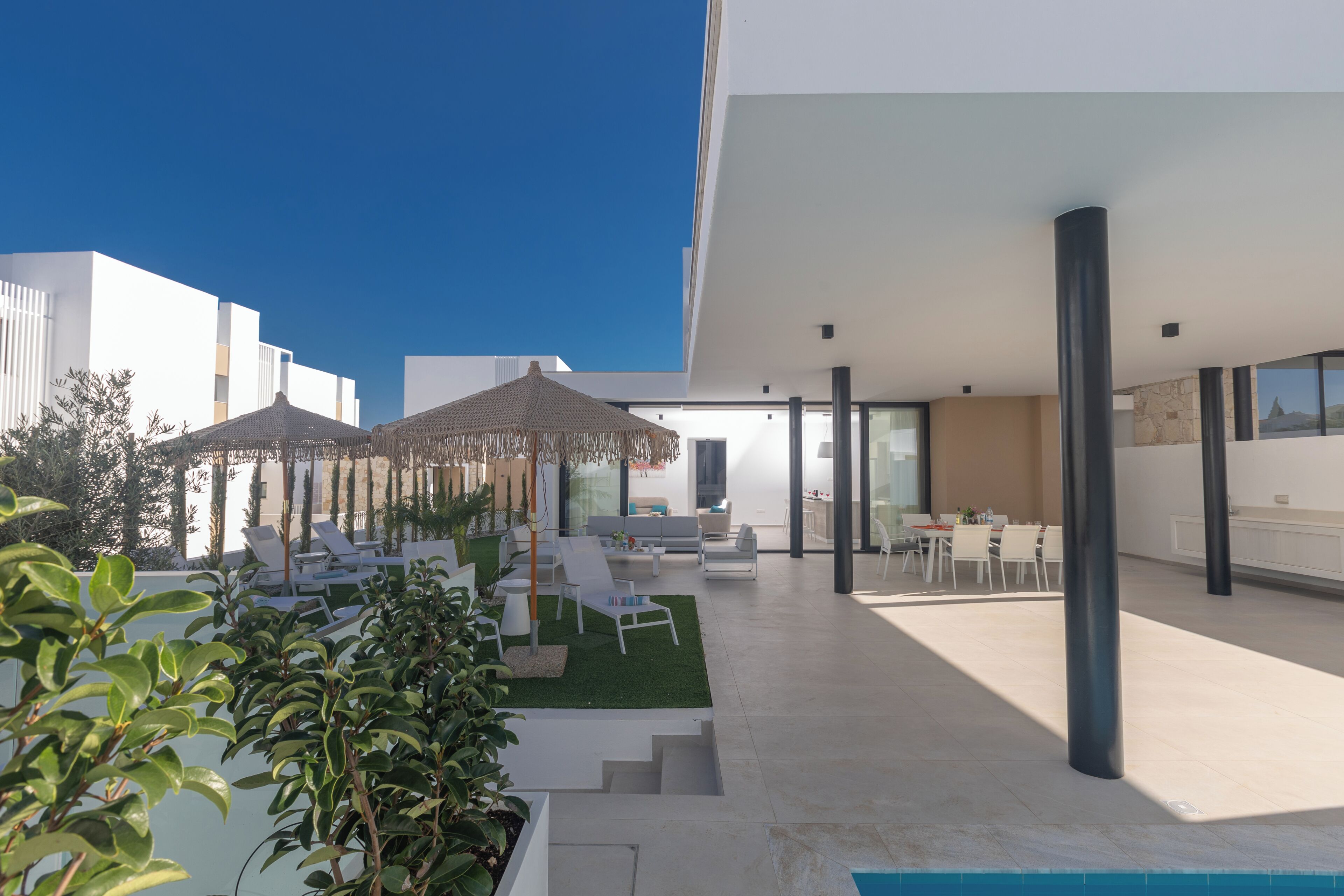 A modern outdoor patio with lounge chairs, umbrellas, and a pool.