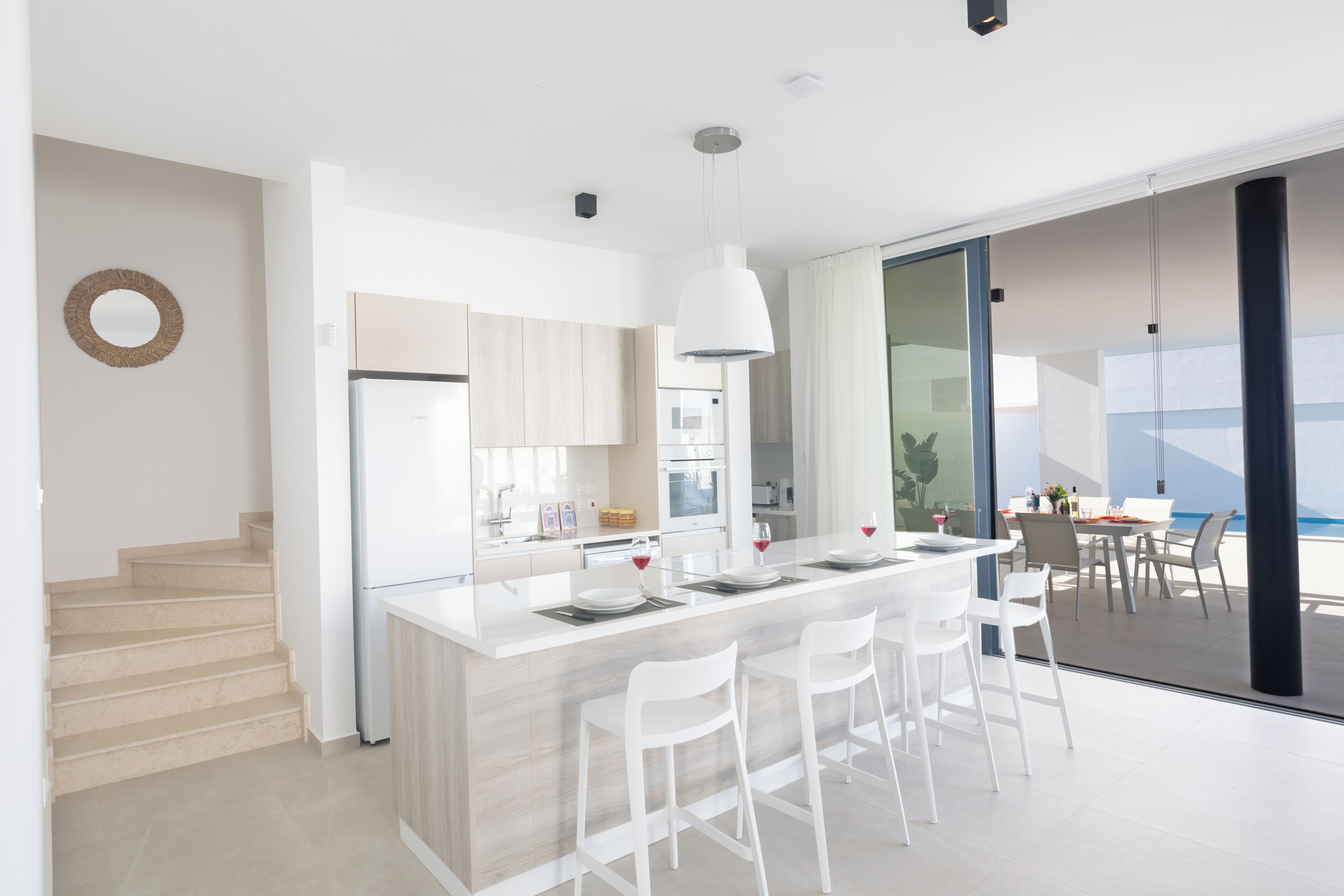 A modern kitchen with a central island, white bar stools, and a dining area with a table and chairs.