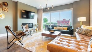 Ein modernes Wohnzimmer mit Ledersofa, Couchtisch, Fernseher und einem großen Fenster mit Blick auf die Stadt.