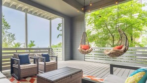 Een overdekt terras met rieten meubilair, hangstoelen en een vloerkleed met geometrisch patroon.