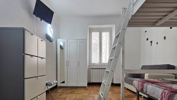 A bedroom with a herringbone wooden floor, a bunk bed, a wardrobe, a TV mounted on the wall, and a window with a curtain. - Cinqueterrehouse (La Spezia)
