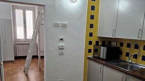 A kitchen with wooden flooring, white cabinets, a yellow and blue backsplash, and a built-in stove. - Cinqueterrehouse (La Spezia)