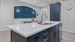 A modern kitchen with a white island, dark cabinets, and a blue accent wall. - Juniper Presents: Beach Bliss Home with Rooftop Deck & Pool Access (Union Pier)