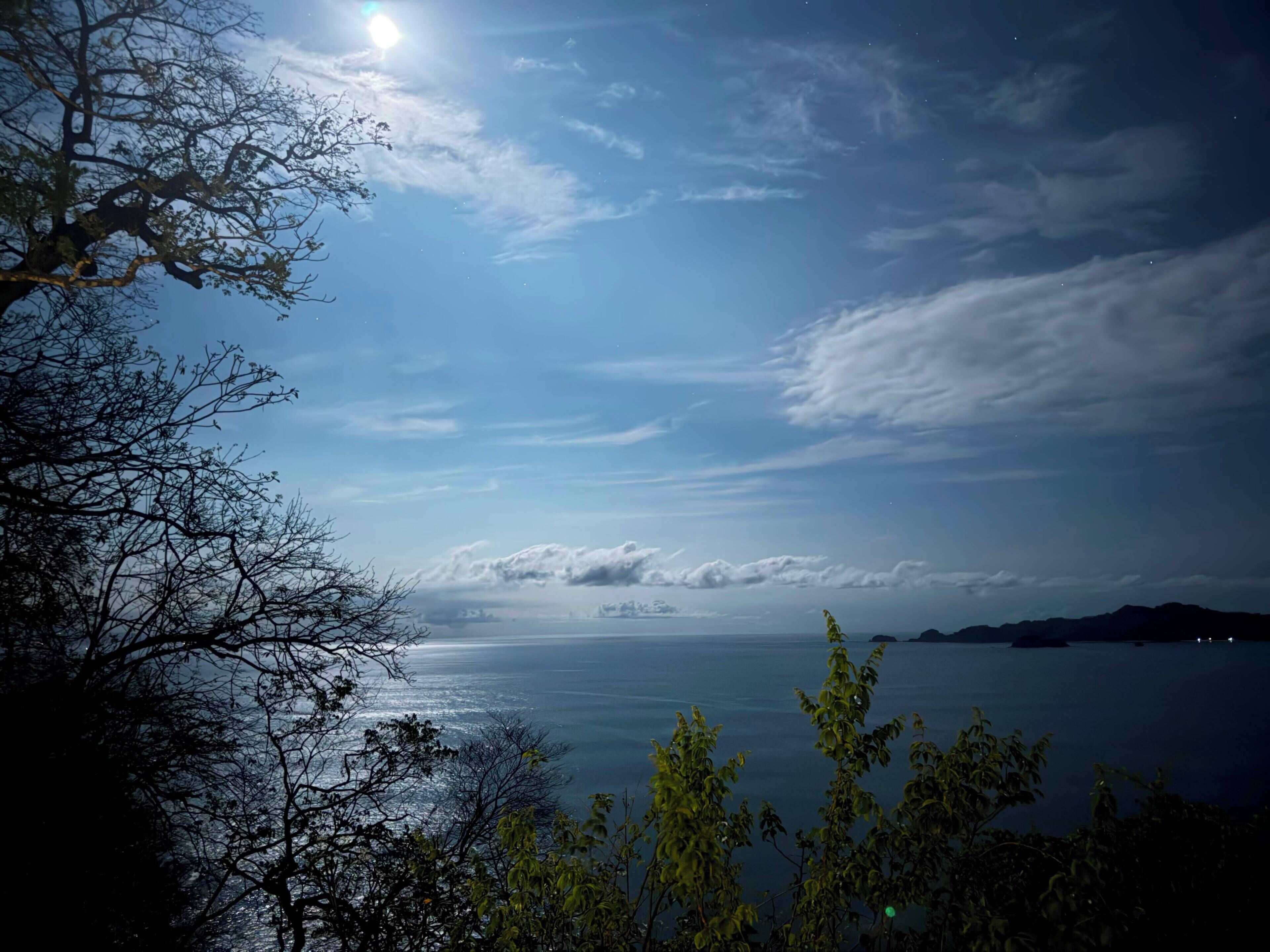 Ein Nachtblick auf eine Küstenregion mit klarem Himmel, einem sichtbaren Mond und ruhiger See.