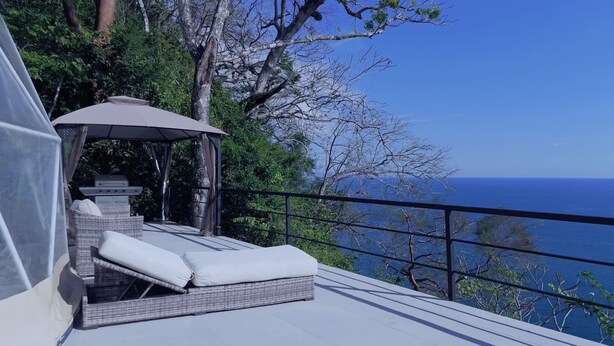 Un balcon doté d’un canapé en osier et d’un auvent, offrant une vue sur une étendue d’eau et un ciel dégagé.