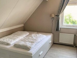 Una habitación pequeña con cama individual, techo inclinado, radiador y ventana con cortinas.
