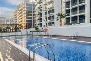A rooftop swimming pool with a wooden deck, surrounded by modern buildings with balconies.