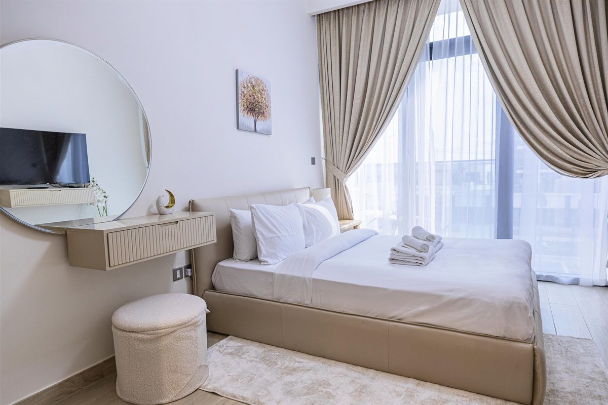 A hotel room with a bed, a round mirror, a television, and a window with curtains.