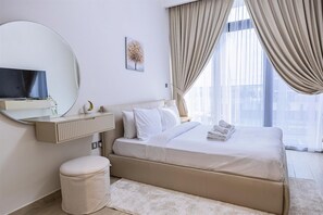 A hotel room with a bed, a round mirror, a television, and a window with curtains. - Upscale Studio Azizi Riviera Prime Location Dubai (Dubai)