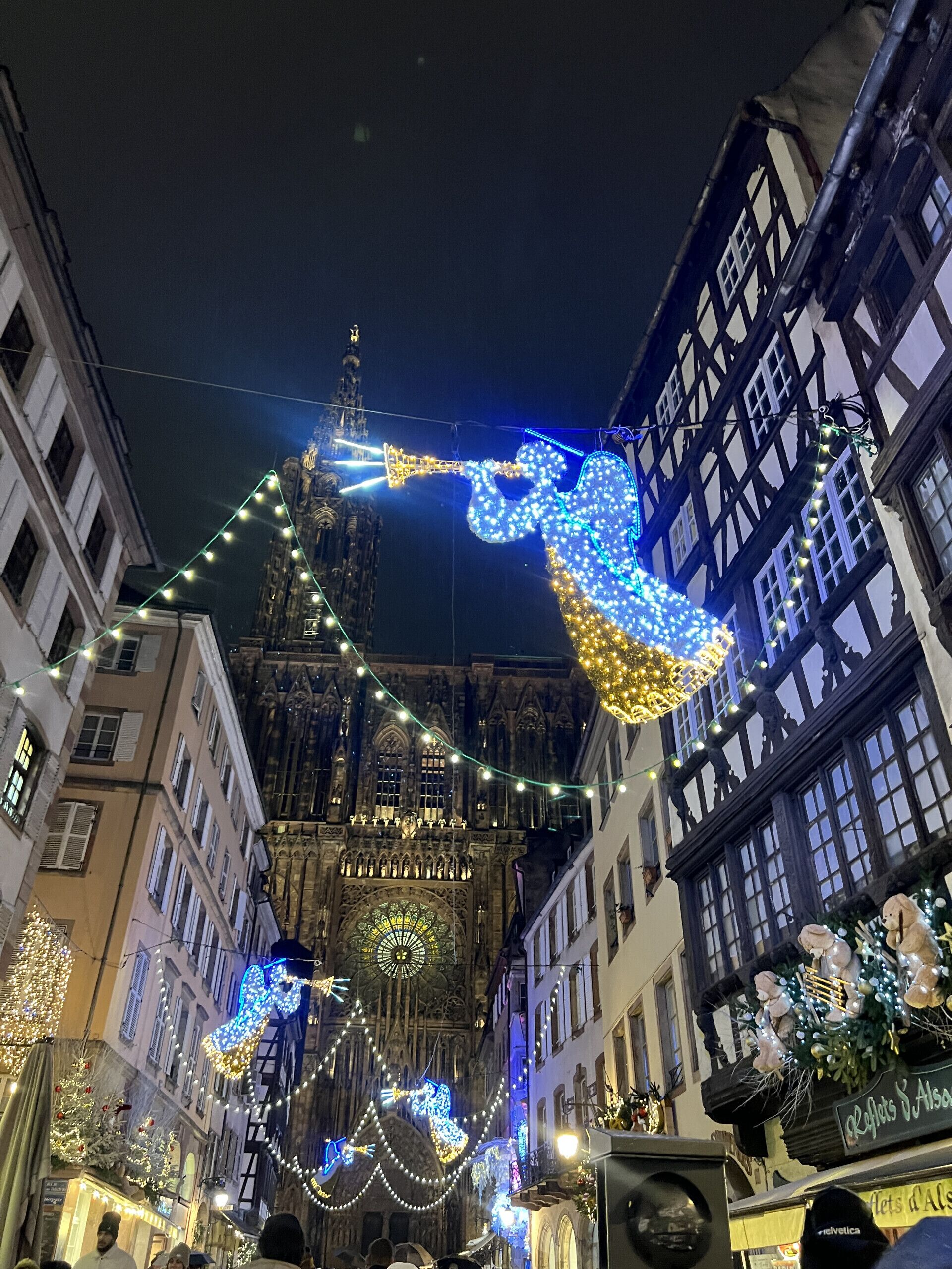 A historic building with intricate architecture, a prominent clock tower, and a festive street decorated with lights and ornaments.