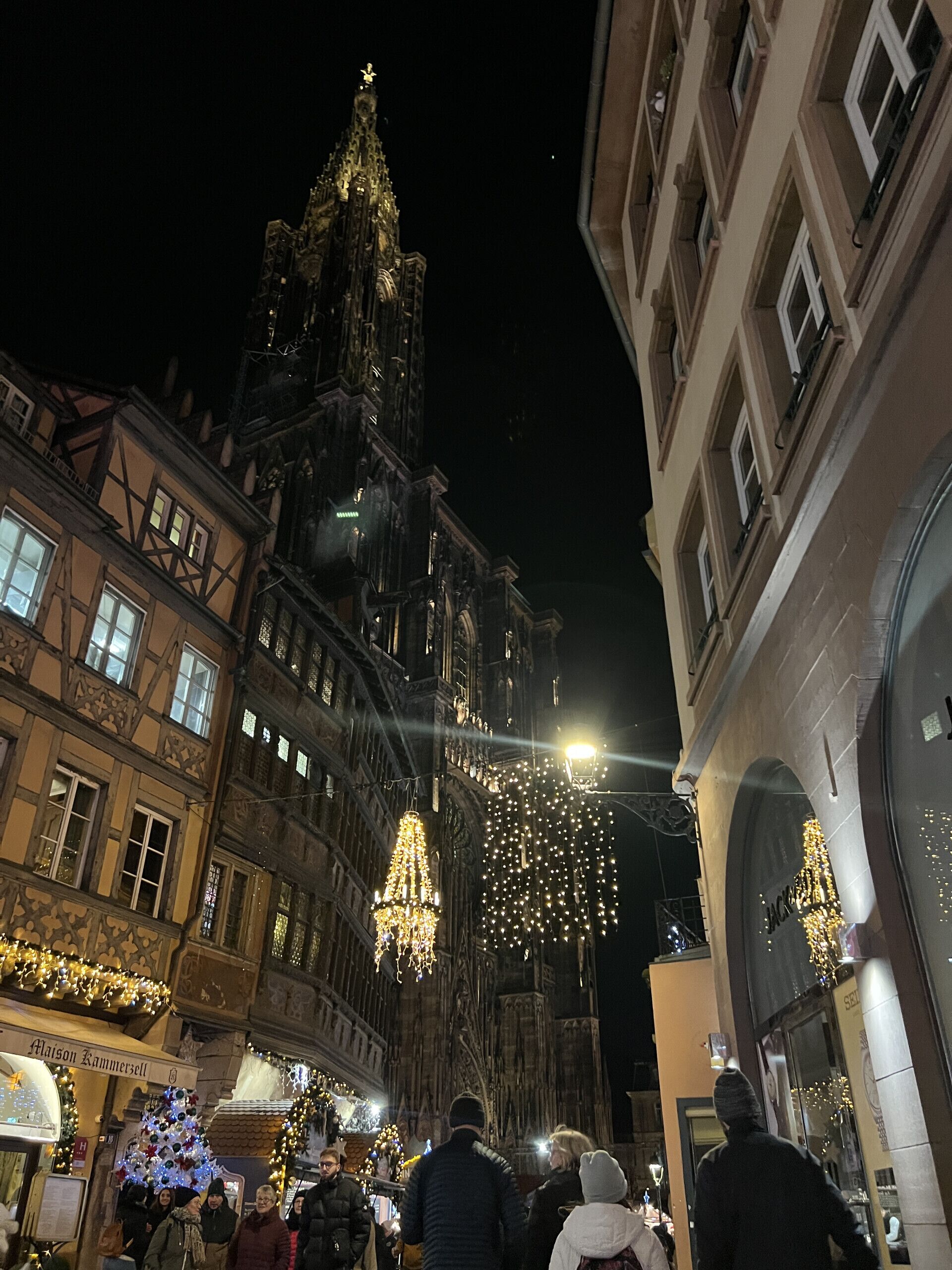 A historic building with intricate architecture, a market area with stalls, and people walking.