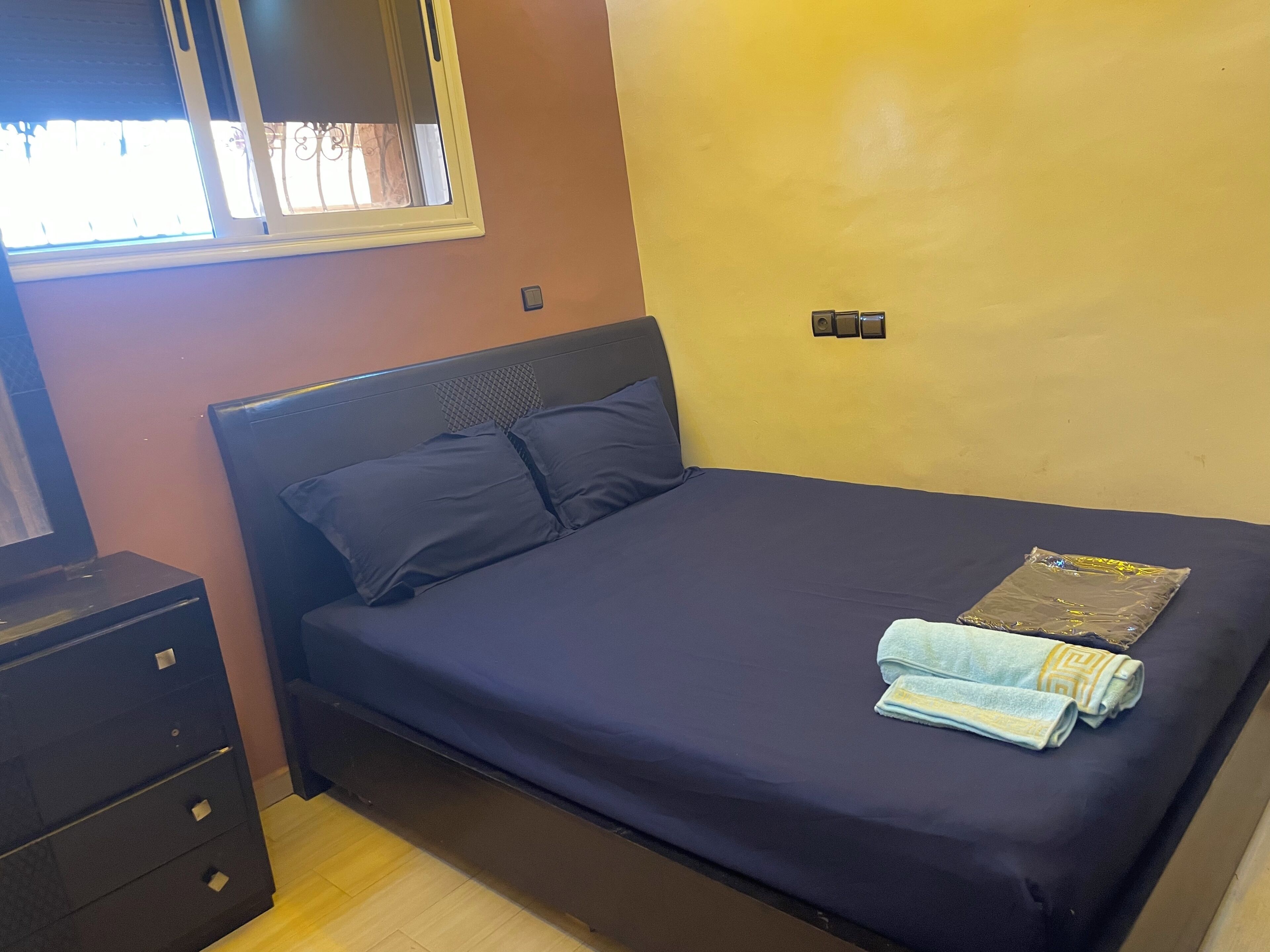 Une chambre à coucher avec un lit, une commode, une fenêtre et un interrupteur mural.