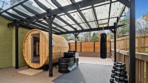 Terraza techada al aire libre con sauna de madera, equipo de ejercicio y saco de boxeo.
