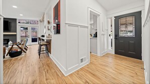 Un interior moderno con piso de madera, una zona de comedor con sillas y una mesa, y una puerta oscura con ventanal.