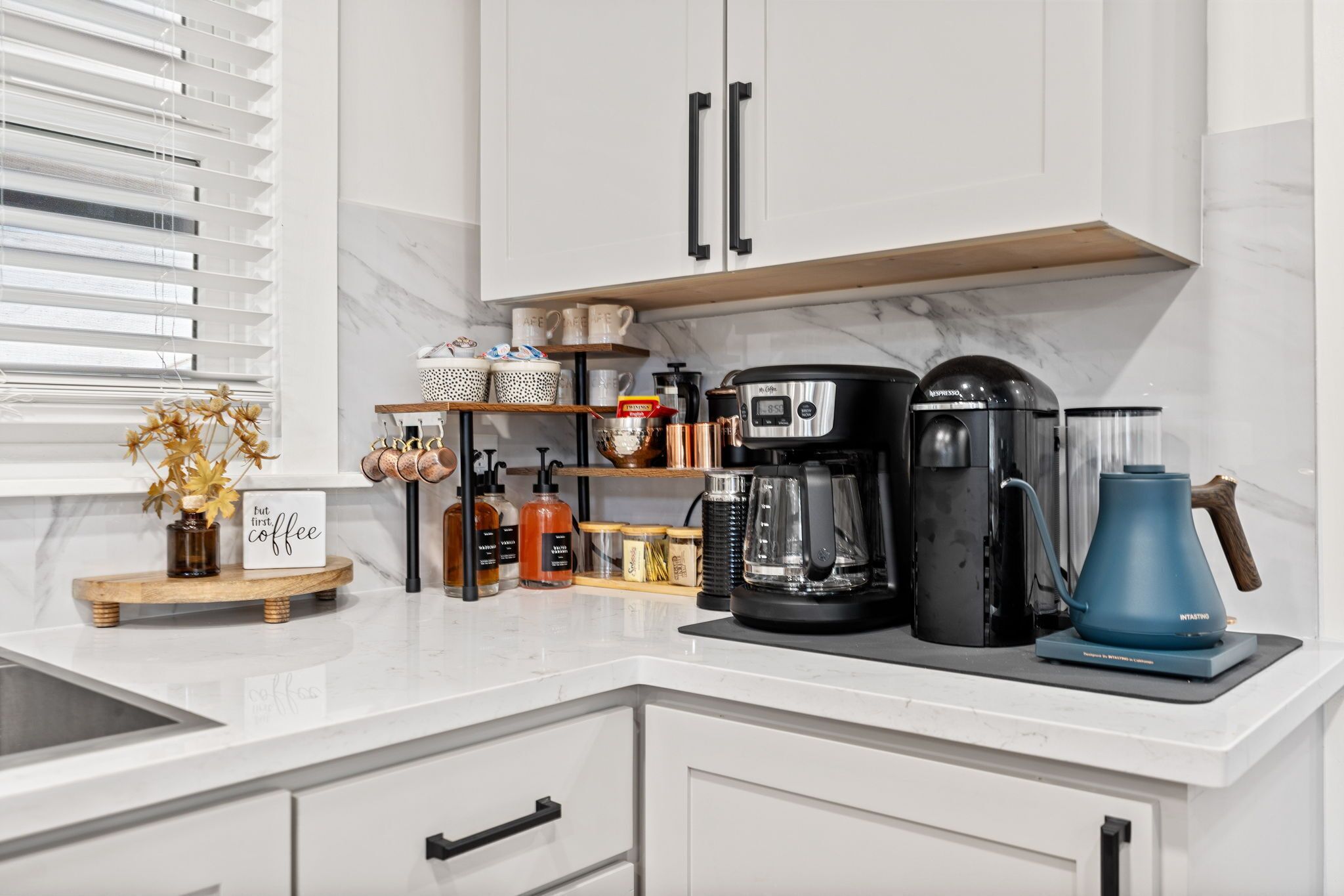 A modern kitchen with white cabinets, a marble countertop, and various appliances including a coffee maker, blender, and kettle.