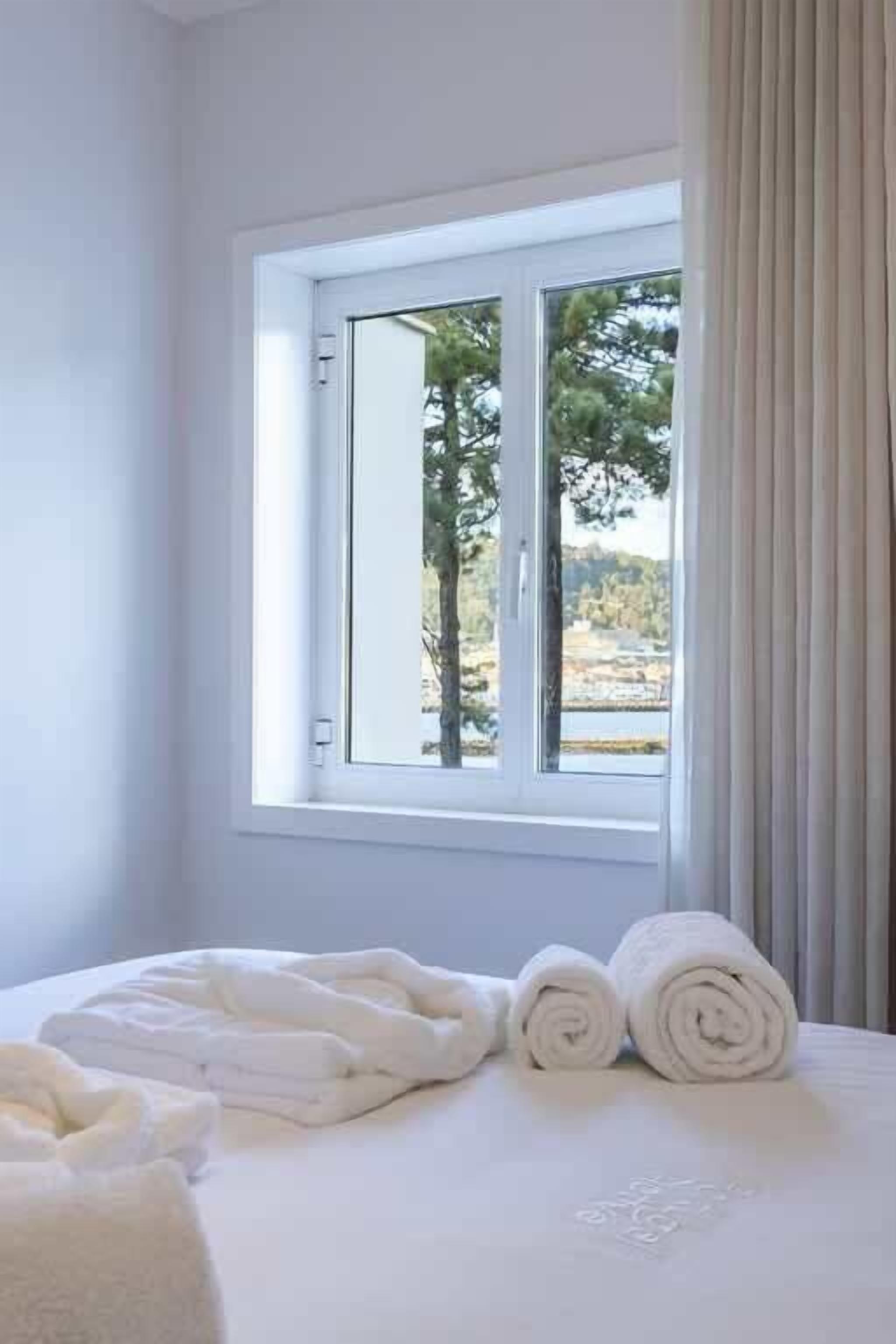 A room with a bed, a window with curtains, and a view of trees and a body of water.