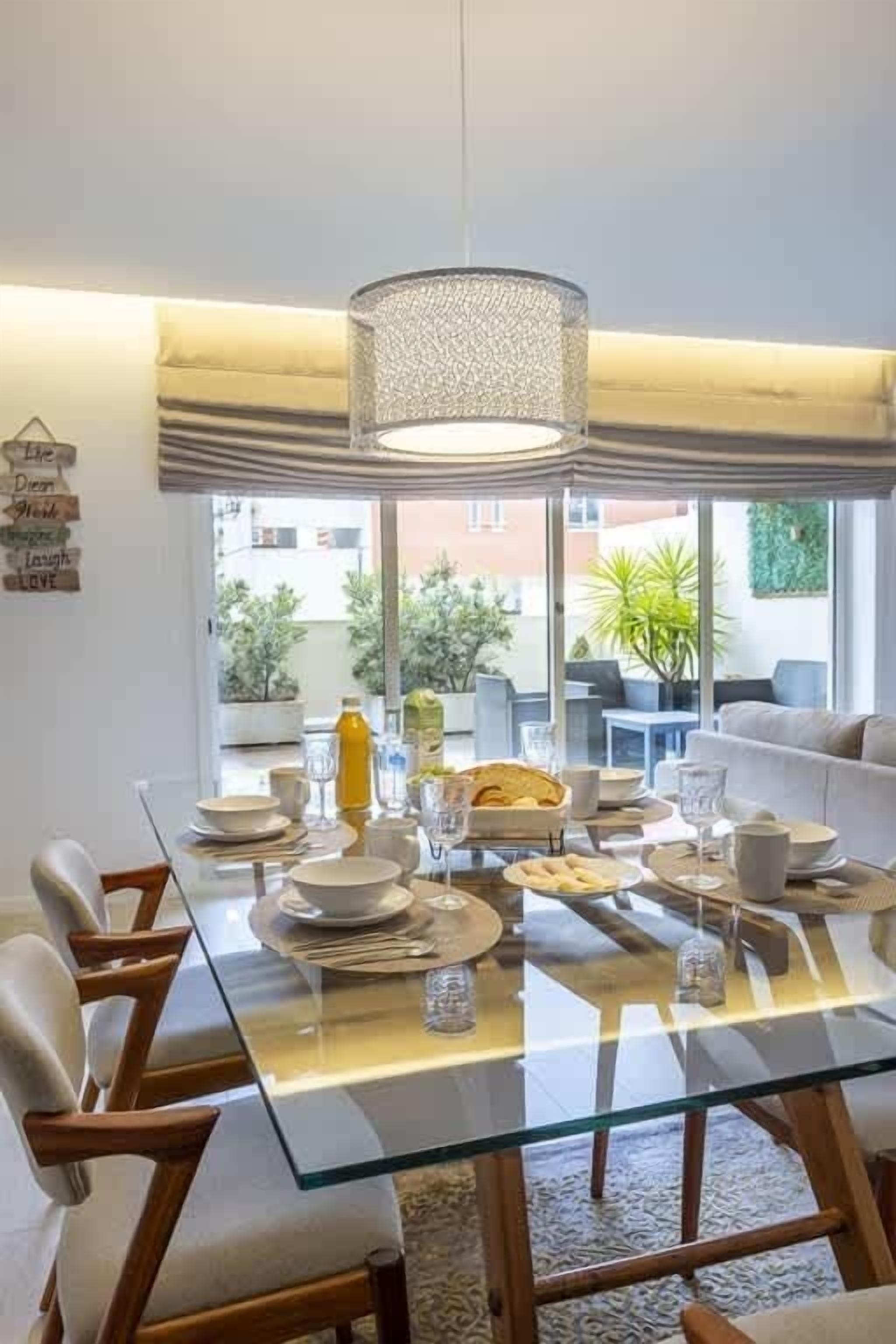 A dining area with a glass table, chairs, and a hanging light fixture.