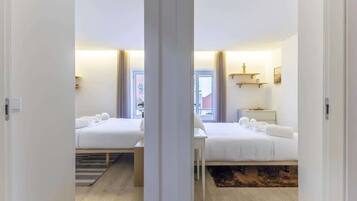 A hotel room with two beds, a bedside table, a nightstand, a window with curtains, and a view of the outside.