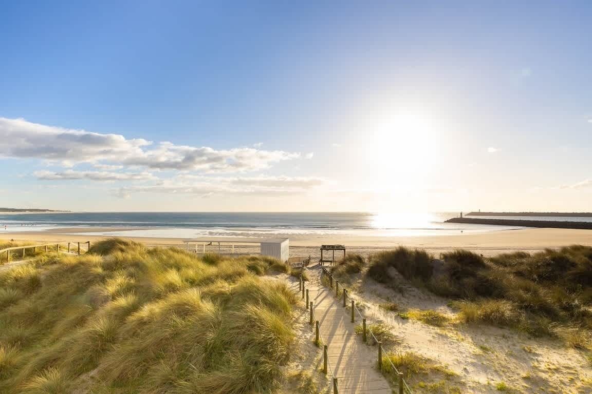 A beach with a wooden walkway, dunes, and a view of the ocean.