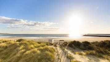 A beach with a wooden walkway, dunes, and a view of the ocean.