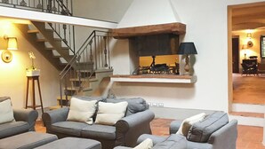 Amplia sala de estar con chimenea, asientos cómodos y una escalera que conduce a un nivel superior.
