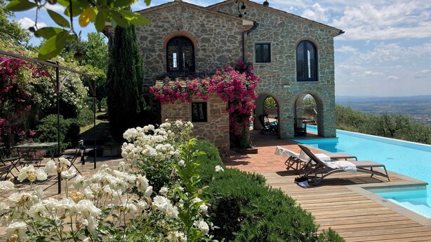 Una villa de piedra con piscina, rodeada de jardines exuberantes y plantas en flor.