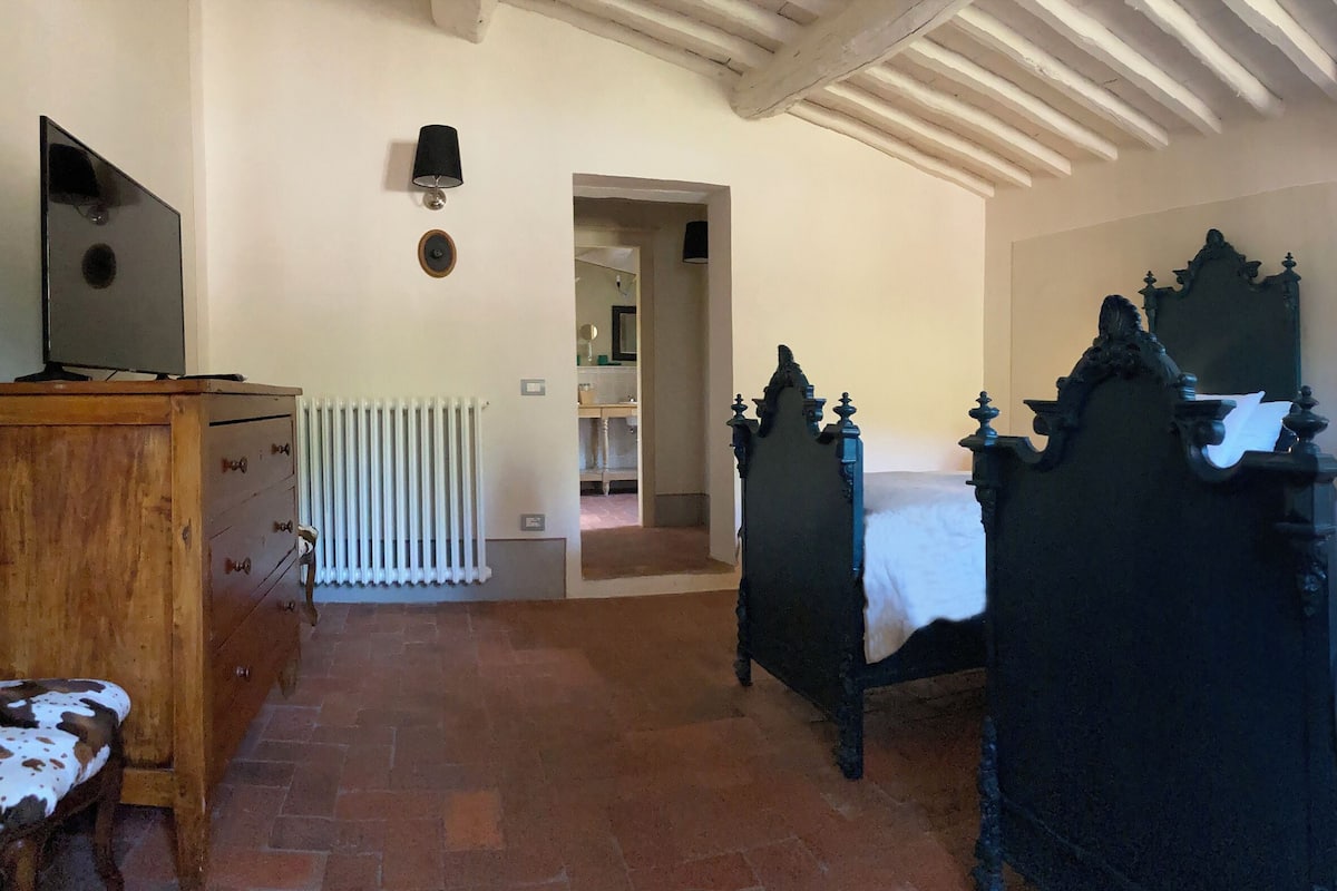 Une chambre à coucher avec un lit à baldaquin, une commode en bois et un téléviseur posé sur un meuble en bois.