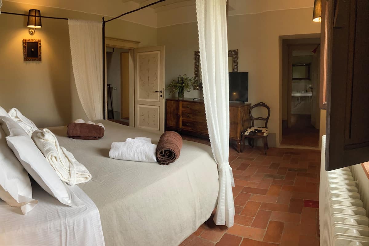 Une chambre à coucher avec un lit, des oreillers, une serviette enroulée, une commode en bois et une chaise.