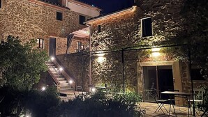 Un edificio de piedra con una escalera que conduce a un balcón, mobiliario exterior y un patio bien iluminado.