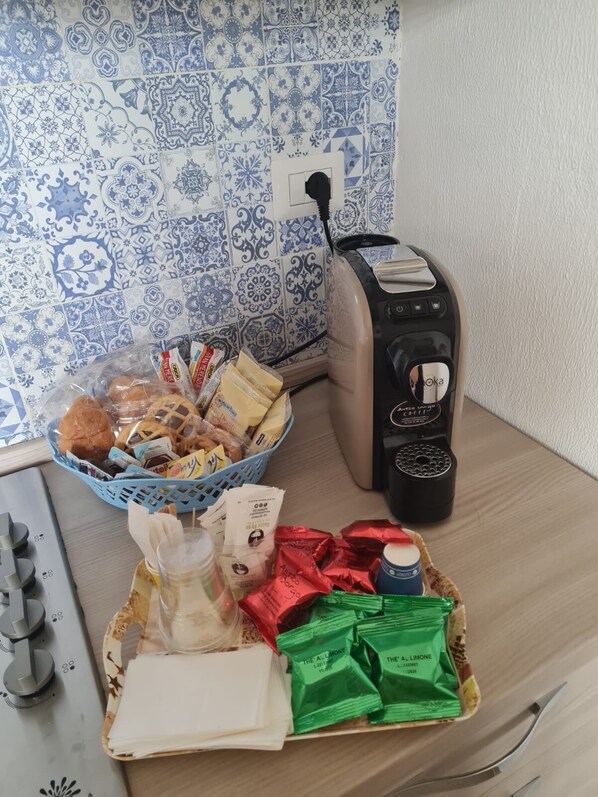 A kitchen counter with a coffee maker, a basket of snacks, and a tray of food items.