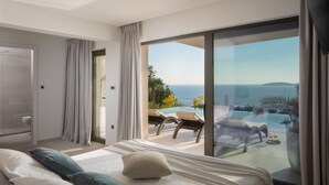 Un dormitorio moderno con una cama grande, vista al mar y un balcón con mobiliario exterior.