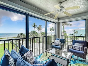 A balcony with a view of the ocean, furnished with a sofa, chairs, and a table.