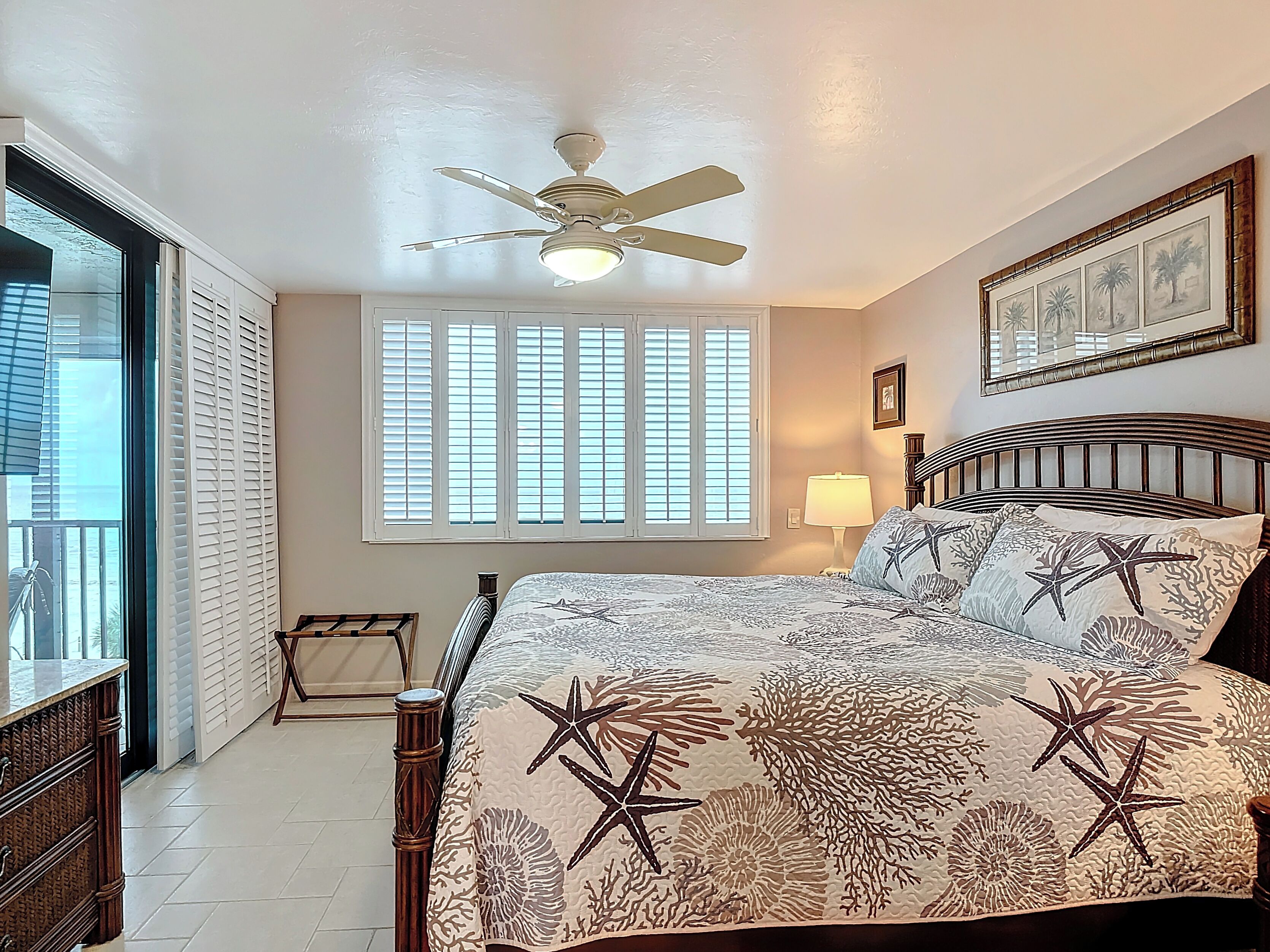 A bedroom with a bed, a ceiling fan, a window with blinds, a nightstand, and a wall-mounted lamp.