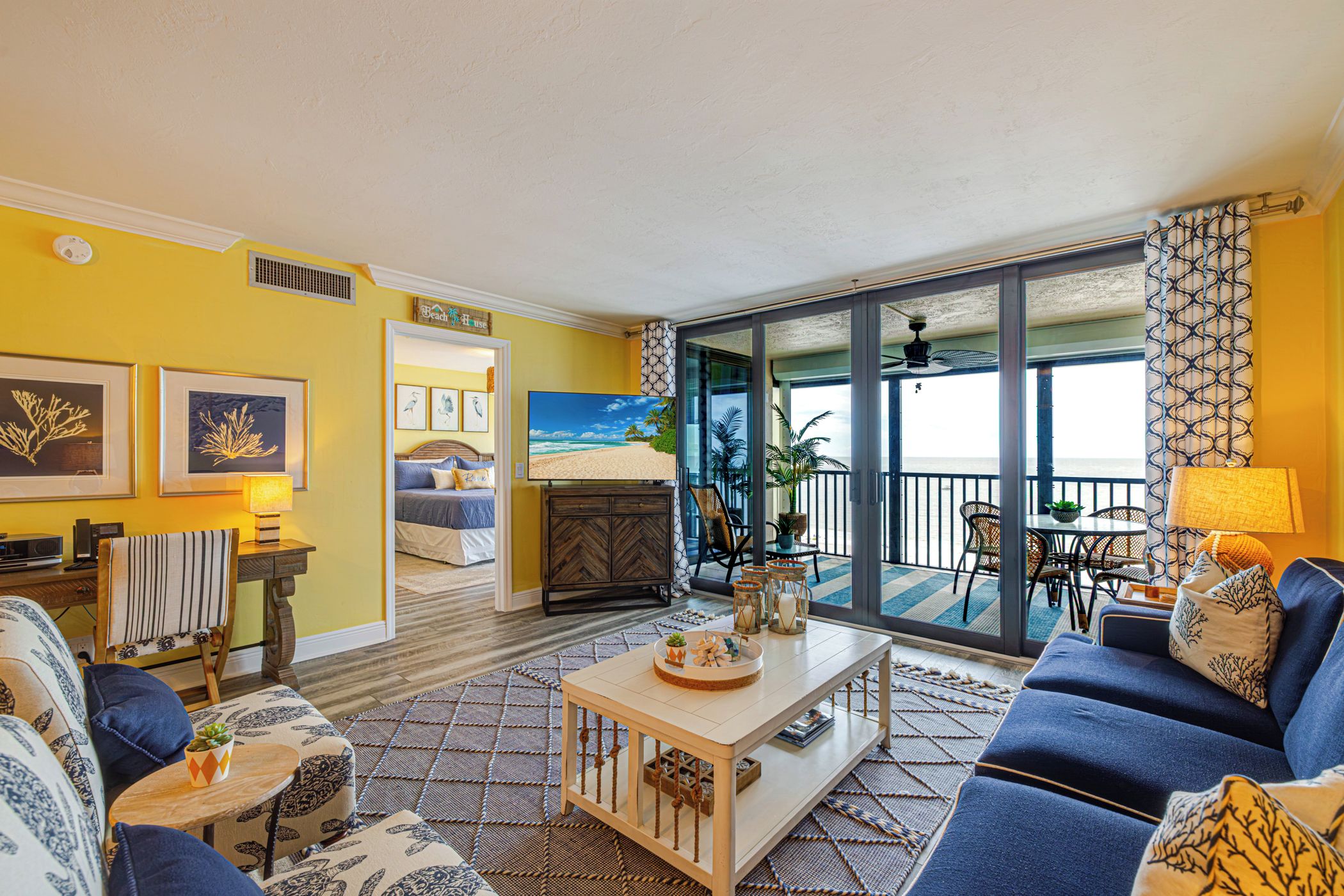 A living room with a sofa, coffee table, and a view of the beach through large glass doors.