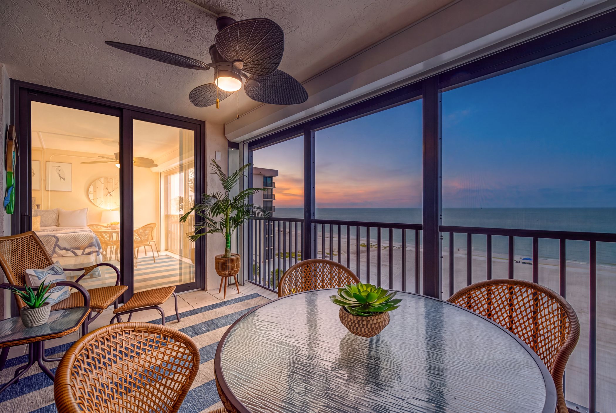 A balcony with a glass table, wicker chairs, and potted plants.